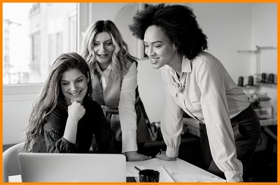 Three dynamic women smiling collaborating on laptop discussing business strategies